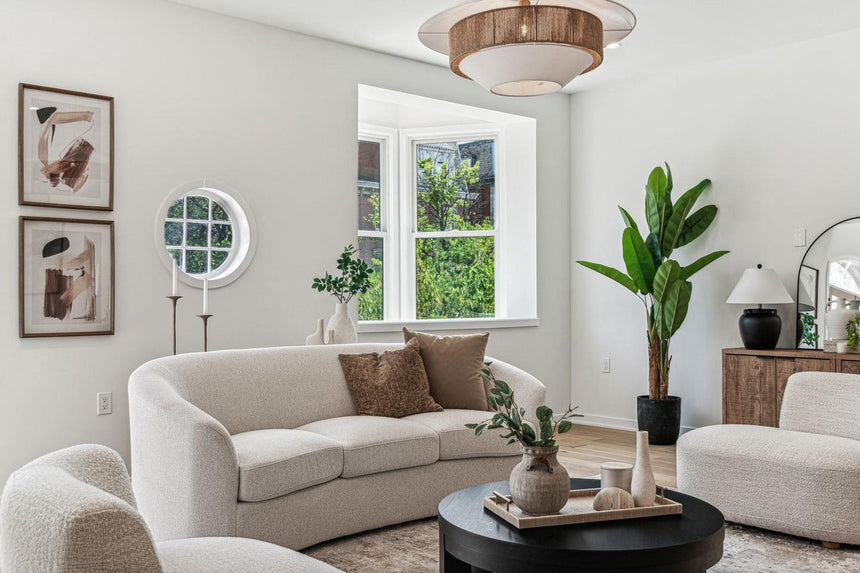 Modern living room in a Philadelphia townhouse featuring curved white sofa, round coffee table, wood sideboard, and large windows with natural light.