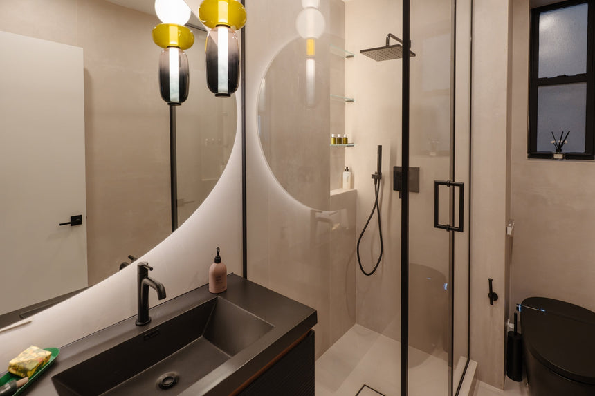 Modern bathroom with a floating wood double-sink vanity, matte black faucets, LED arched mirrors, and a frameless glass shower.