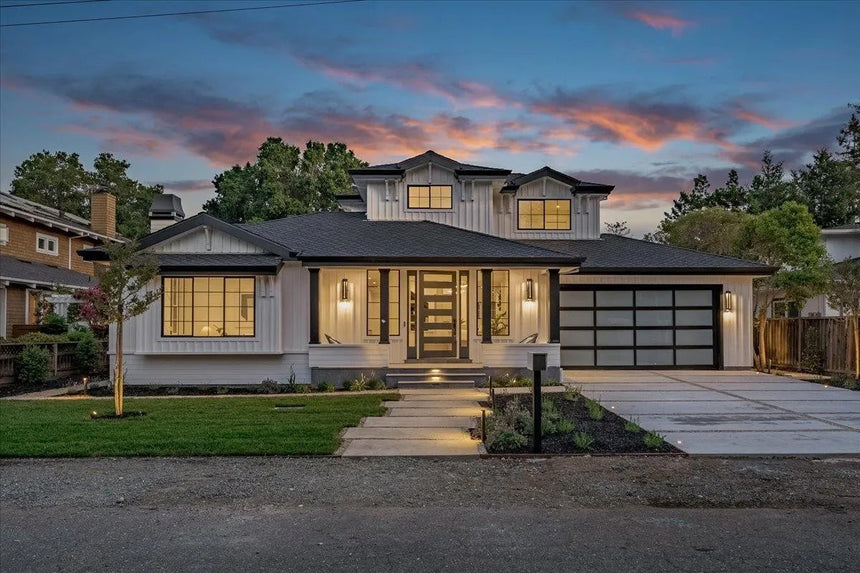 Modern farmhouse front exterior at dusk with black framed windows, covered porch, and illuminated pathway