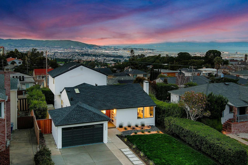 Modern mid-century home exterior with large glass garage doors, sloped roofline, and landscaped front yard at sunset.
