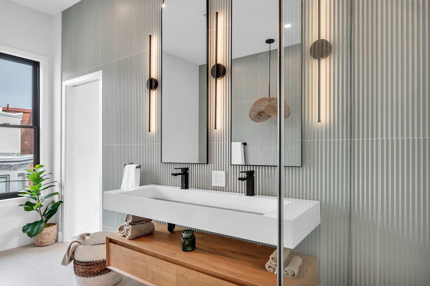 Modern bathroom with a floating wood double-sink vanity, matte black faucets, LED arched mirrors, and a frameless glass shower.