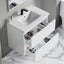 Bathroom vanity with open drawer displaying toiletries on a marble floor.