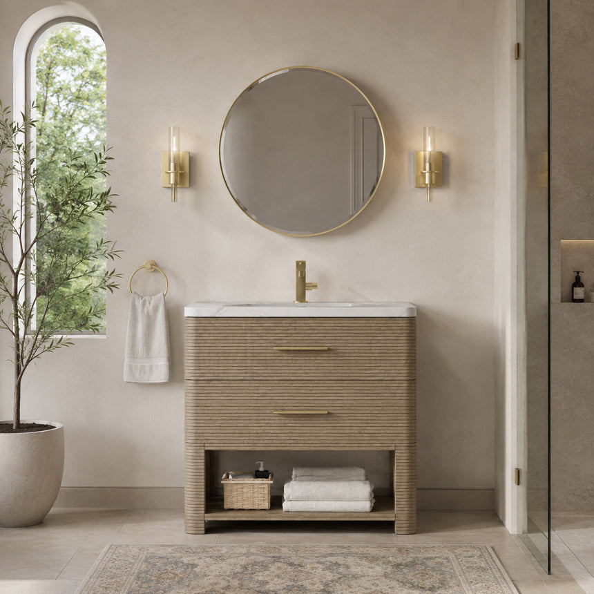 A modern bathroom vanity with a light oak wood frame, six drawers, an open lower shelf, and a white marble top with an integrated sink. The vanity is styled in a bright bathroom with a white freestanding tub, a gold faucet, and a glass shower stall in the background.