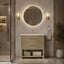 A modern bathroom vanity with a woven natural-fiber cabinet, white sink basin, and gold faucet, styled in a warm, contemporary bathroom setting with a round backlit mirror, wall sconces, and a towel ring.