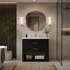A modern bathroom vanity setup featuring a black textured cabinet with gold handles, a white countertop, a gold faucet, a round gold-framed mirror, and matching wall sconces, set in a styled bathroom interior.