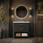 A modern bathroom vanity setup with a dark textured cabinet, white countertop, gold faucet, round backlit mirror, and matching wall sconces in a dark stone bathroom.