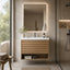 A modern floating bathroom vanity with a white countertop and sink, a wood-look slatted cabinet, and an open lower shelf, shown in a minimalist bathroom setting with a matching backlit mirror and a glass shower enclosure.