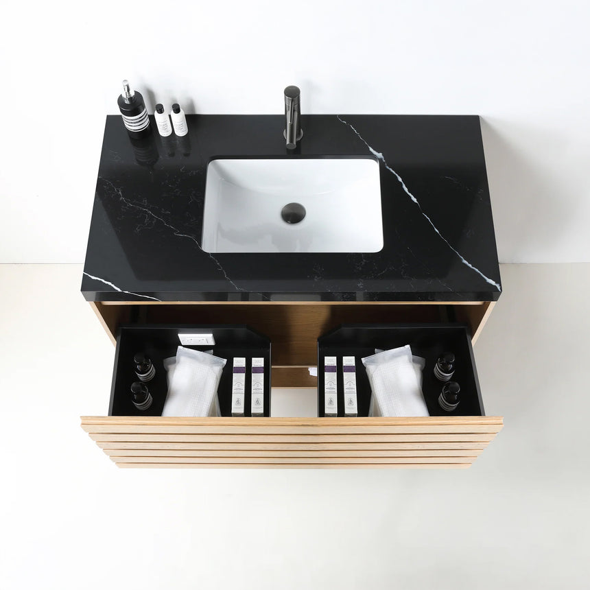 A modern floating bathroom vanity with a light oak wood finish, a white countertop, and an integrated sink, shown in a styled bathroom setting with a bathtub, shower glass, and decorative plants.