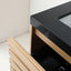 Close-up of a modern vanity or cabinet with a glossy black countertop, light natural wood frame, and an open drawer showing dark interior storage.