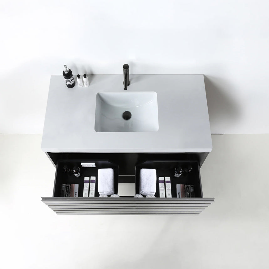 A modern floating bathroom vanity with a light oak wood finish, a white countertop, and an integrated sink, shown in a styled bathroom setting with a bathtub, shower glass, and decorative plants.