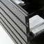 Close-up of a dark gray drawer front with a grooved, modern design, partially open to reveal a black interior containing a white textured item and a box.