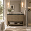 A modern bathroom vanity with a textured light brown wood cabinet, a black countertop, and a gold faucet, set in a bright, contemporary bathroom with a mirror, wall sconces, and a glass shower door.