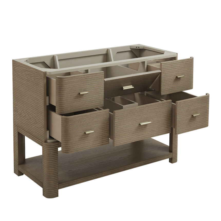 A modern bathroom vanity with a light oak wood frame, six drawers, an open lower shelf, and a white marble top with an integrated sink. The vanity is styled in a bright bathroom with a white freestanding tub, a gold faucet, and a glass shower stall in the background.