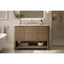 A modern bathroom vanity with a light oak wood frame, six drawers, an open lower shelf, and a white marble top with an integrated sink. The vanity is styled in a bright bathroom with a white freestanding tub, a gold faucet, and a glass shower stall in the background.
