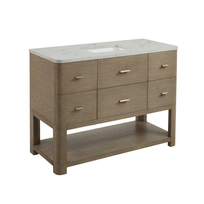A modern bathroom vanity with a light oak wood frame, six drawers, an open lower shelf, and a white marble top with an integrated sink. The vanity is styled in a bright bathroom with a white freestanding tub, a gold faucet, and a glass shower stall in the background.