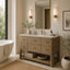 A modern bathroom vanity with a light wood cabinet, white marble countertop, and a large rectangular mirror, shown in a styled bathroom setting with a freestanding tub, wall sconces, and plants.