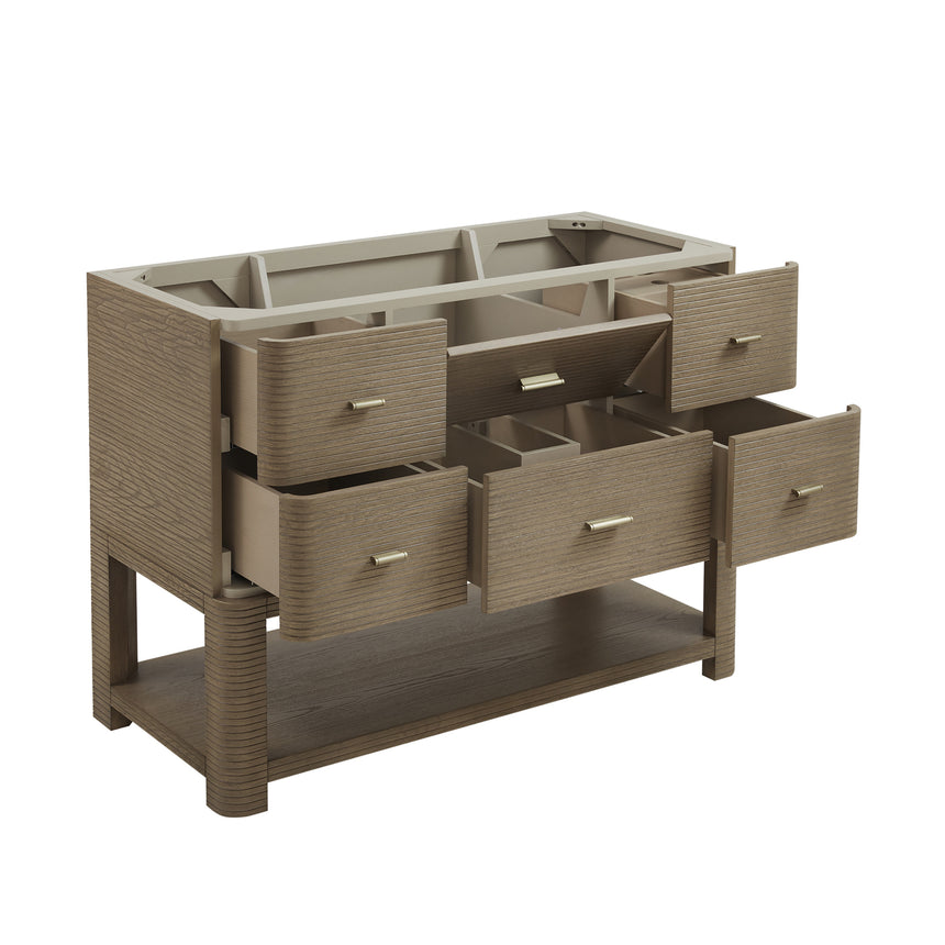 A modern bathroom vanity with a light oak wood frame, six drawers, an open lower shelf, and a white marble top with an integrated sink. The vanity is styled in a bright bathroom with a white freestanding tub, a gold faucet, and a glass shower stall in the background.