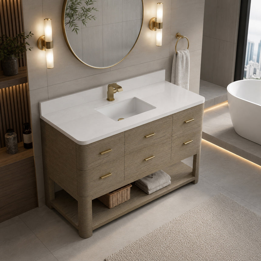 A modern bathroom vanity with a light oak wood frame, six drawers, an open lower shelf, and a white marble top with an integrated sink. The vanity is styled in a bright bathroom with a white freestanding tub, a gold faucet, and a glass shower stall in the background.