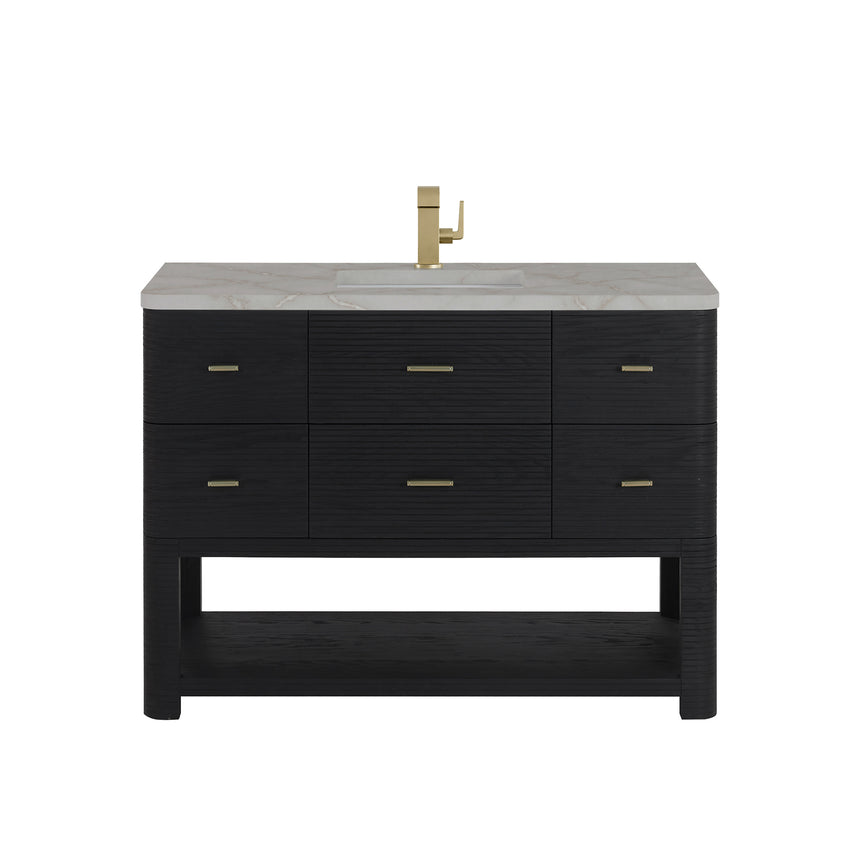 A modern bathroom vanity with a light oak wood frame, six drawers, an open lower shelf, and a white marble top with an integrated sink. The vanity is styled in a bright bathroom with a white freestanding tub, a gold faucet, and a glass shower stall in the background.