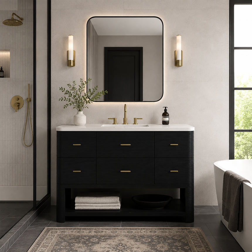 A modern bathroom vanity with a light oak wood frame, six drawers, an open lower shelf, and a white marble top with an integrated sink. The vanity is styled in a bright bathroom with a white freestanding tub, a gold faucet, and a glass shower stall in the background.