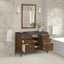 Bathroom vanity with open drawers, mirror, and decorative elements against a tiled wall.