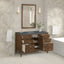 Bathroom vanity with open drawers, mirror, and decorative elements against a tiled wall.