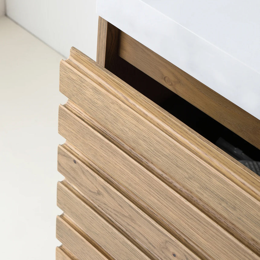 A modern floating bathroom vanity with a light oak wood finish, a white countertop, and an integrated sink, shown in a styled bathroom setting with a bathtub, shower glass, and decorative plants.