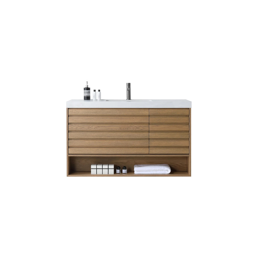 A modern floating bathroom vanity with a light oak wood finish, a white countertop, and an integrated sink, shown in a styled bathroom setting with a bathtub, shower glass, and decorative plants.
