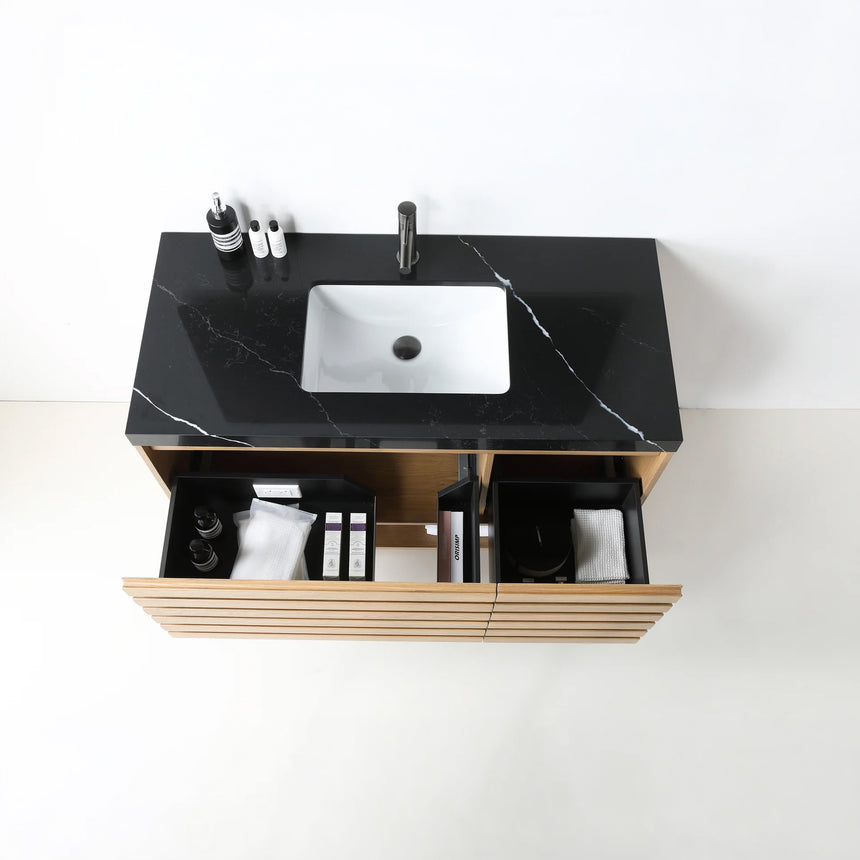 A modern floating bathroom vanity with a light oak wood finish, a white countertop, and an integrated sink, shown in a styled bathroom setting with a bathtub, shower glass, and decorative plants.