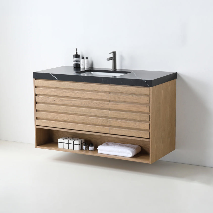 A modern floating bathroom vanity with a light oak wood finish, a white countertop, and an integrated sink, shown in a styled bathroom setting with a bathtub, shower glass, and decorative plants.