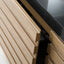 Close-up of a modern kitchen cabinet with light oak wood slatted doors and a black stone countertop.