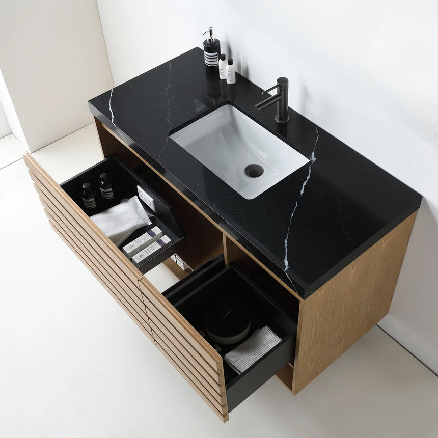 A modern floating bathroom vanity with a light oak wood finish, a white countertop, and an integrated sink, shown in a styled bathroom setting with a bathtub, shower glass, and decorative plants.