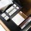A close-up of a drawer organizer containing skincare products, including two white cartons with purple accents, two small white boxes, a white tray, and a pink-and-white ORISIMP box, arranged on a dark tray.