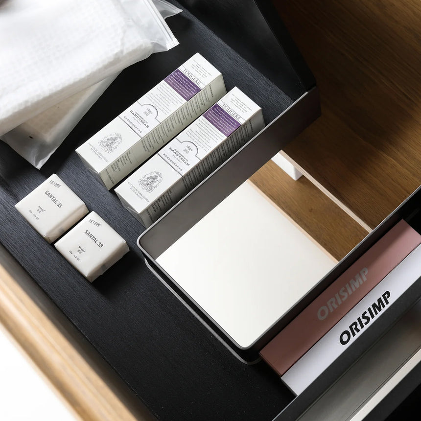 A modern floating bathroom vanity with a light oak wood finish, a white countertop, and an integrated sink, shown in a styled bathroom setting with a bathtub, shower glass, and decorative plants.