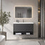 A modern floating bathroom vanity with a white rectangular sink, dark gray slatted cabinet, open lower shelf with folded towels, and a matching backlit rectangular mirror above on a light gray wall.