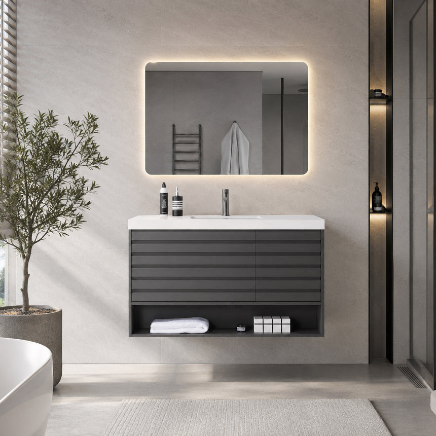A modern floating bathroom vanity with a light oak wood finish, a white countertop, and an integrated sink, shown in a styled bathroom setting with a bathtub, shower glass, and decorative plants.