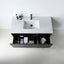 A modern wall-mounted bathroom vanity with a white rectangular sink, matte black faucet, and open lower drawer showing toiletries, photographed from above against a clean white wall and light floor.