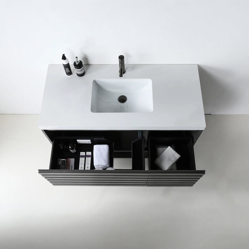 A modern floating bathroom vanity with a light oak wood finish, a white countertop, and an integrated sink, shown in a styled bathroom setting with a bathtub, shower glass, and decorative plants.