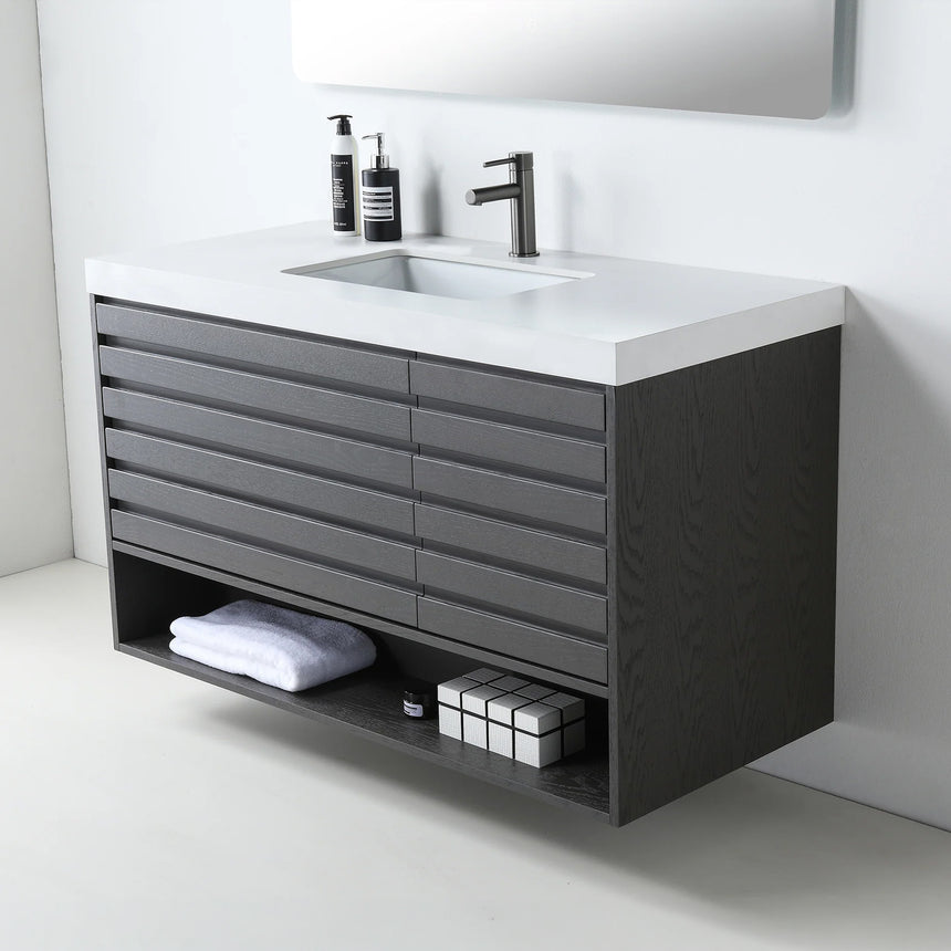 A modern floating bathroom vanity with a light oak wood finish, a white countertop, and an integrated sink, shown in a styled bathroom setting with a bathtub, shower glass, and decorative plants.