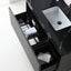 A modern black vanity cabinet with two open drawers, showing toiletries and folded towels, next to a white rectangular sink on a black countertop.