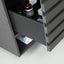 Close-up of a dark gray wooden drawer with a pull handle, partially open to reveal a storage compartment inside containing bottles and a folded white item.