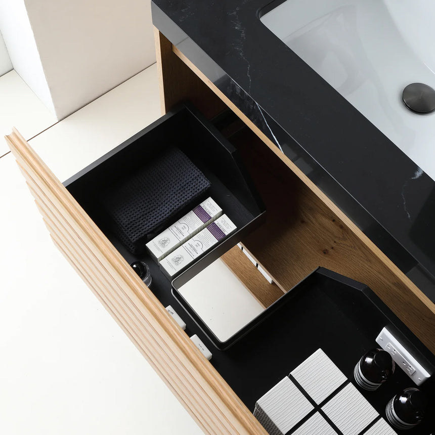 A modern floating bathroom vanity with a light oak wood finish, a white countertop, and an integrated sink, shown in a styled bathroom setting with a bathtub, shower glass, and decorative plants.