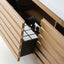 A close-up of a light natural wood vanity or cabinet drawer with a black pull-out organizer inside, holding two small amber bottles and a white tray.