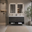 A modern floating bathroom vanity with a dark charcoal gray slatted cabinet, integrated white sink, and two backlit rectangular mirrors mounted on a textured light gray wall. A glass shower door is visible on the left, and a potted plant stands on the right.