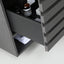 Close-up of a dark gray wooden drawer with a pull handle, partially open to reveal a shelf inside containing bottles and a folded white cloth.