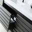 A close-up of a modern bathroom vanity with dark charcoal gray slatted drawers and a white countertop. One drawer is open, revealing a black organizer pocket holding a white electrical outlet cover and a boxed item.