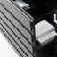 Close-up of a dark gray drawer with horizontal grooved lines, partially open to reveal white storage bins and items inside.