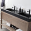 Bathroom vanity with black countertop, double sinks, and wooden cabinets.