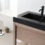 Bathroom vanity with black countertop and faucet, wooden cabinet, and small plant.