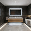 Modern bathroom with dark marble walls, wooden vanity, and illuminated mirror.